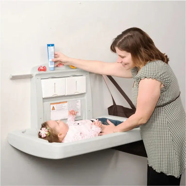 Dolphy Horizontal Baby Change Station – lifestyle in-use view showing caregiver changing infant on wall-mounted station in public restroom